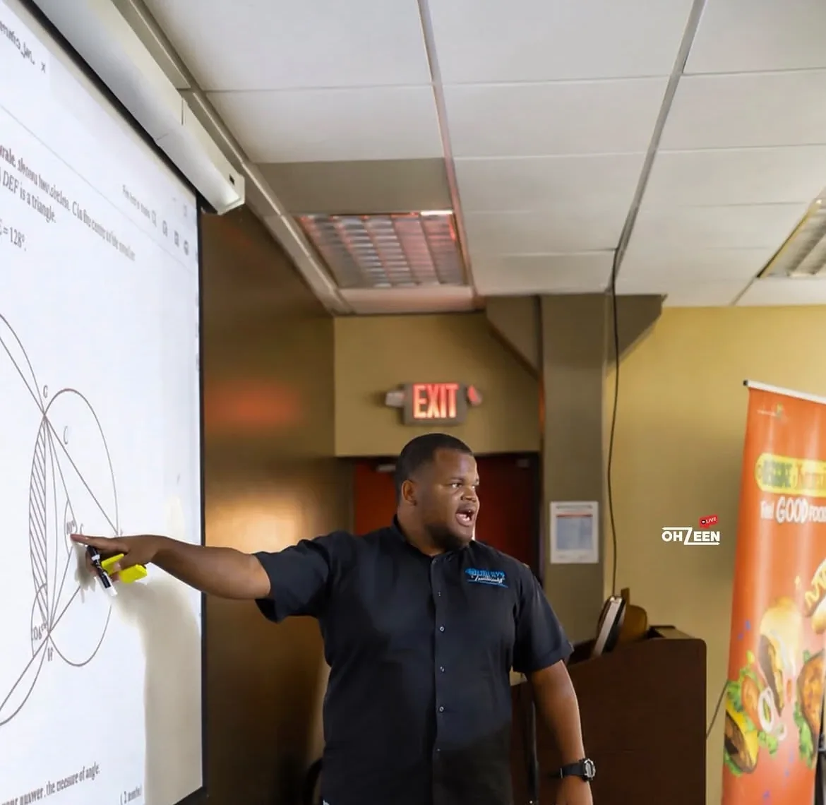 Founder Demar Hemley teaching a CSEC mathematics session, pointing to a geometry question on a projector screen